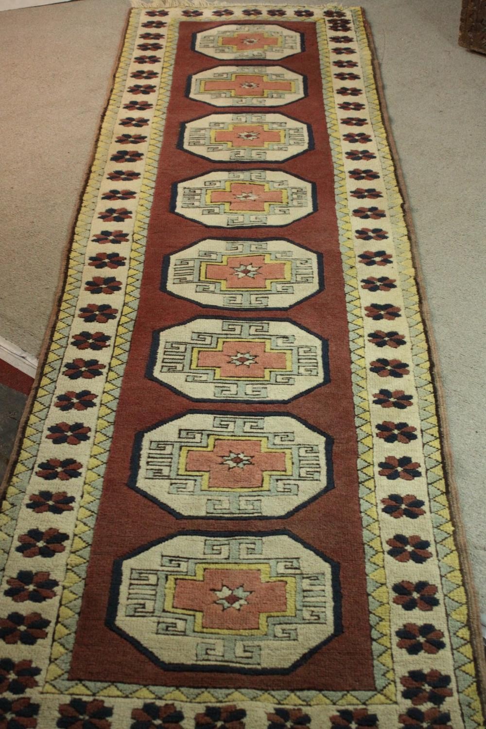 A Turkish runner with repeating lozenge medallions within a flowerhead border. L.310 W.30cm.