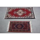 Two small Eastern rugs each on a red ground. L.110 W.60cm. (largest)