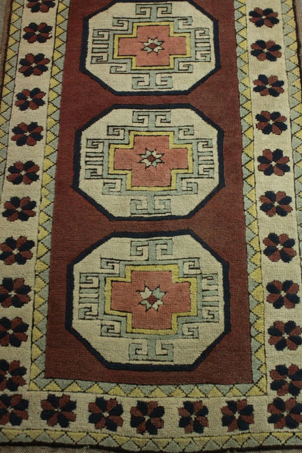 A Turkish runner with repeating lozenge medallions within a flowerhead border. L.310 W.30cm. - Image 3 of 7