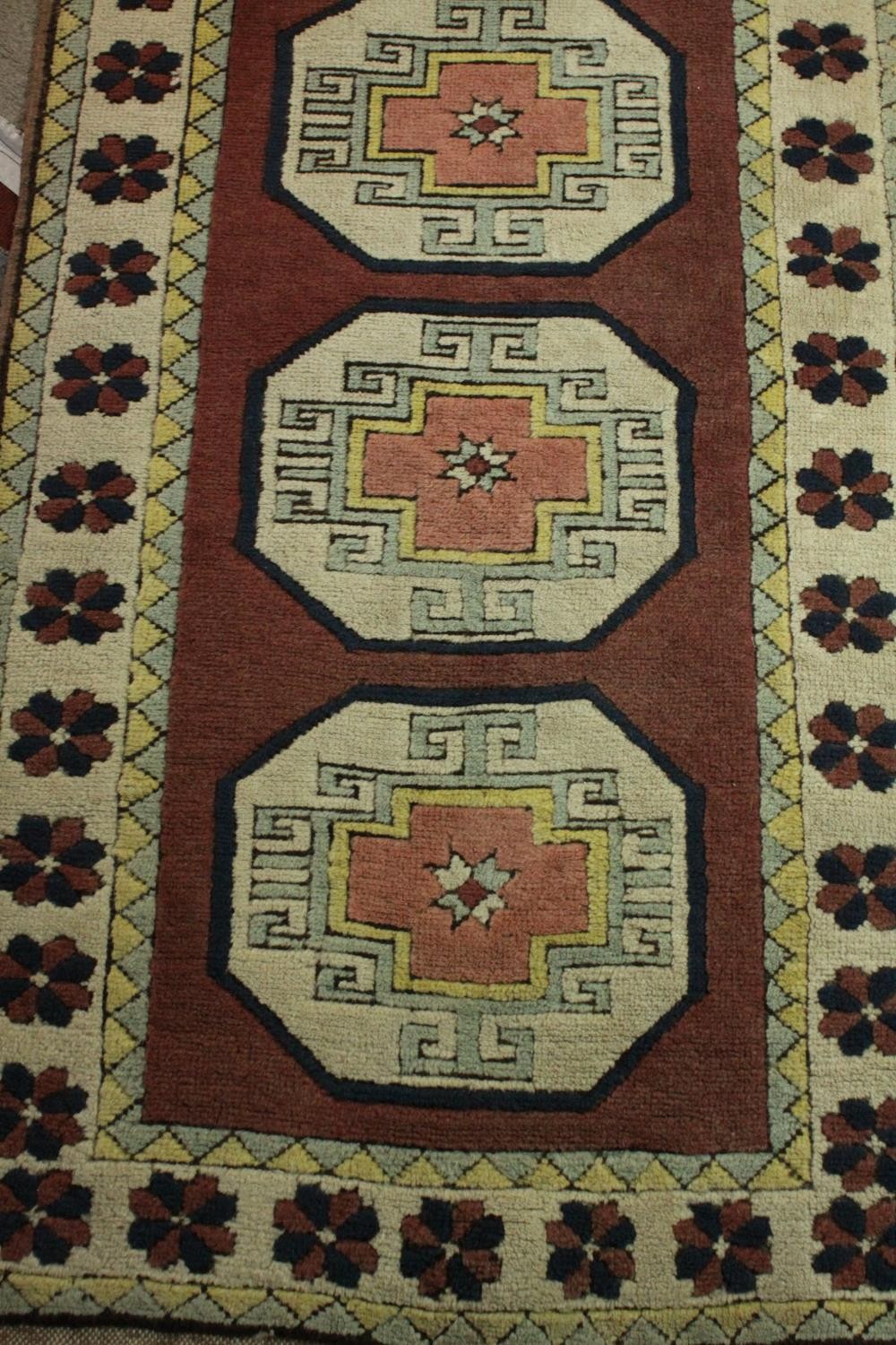 A Turkish runner with repeating lozenge medallions within a flowerhead border. L.310 W.30cm. - Image 2 of 7