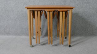 A vintage light teak nest of tables on beech supports fitted with three slide out drop flap