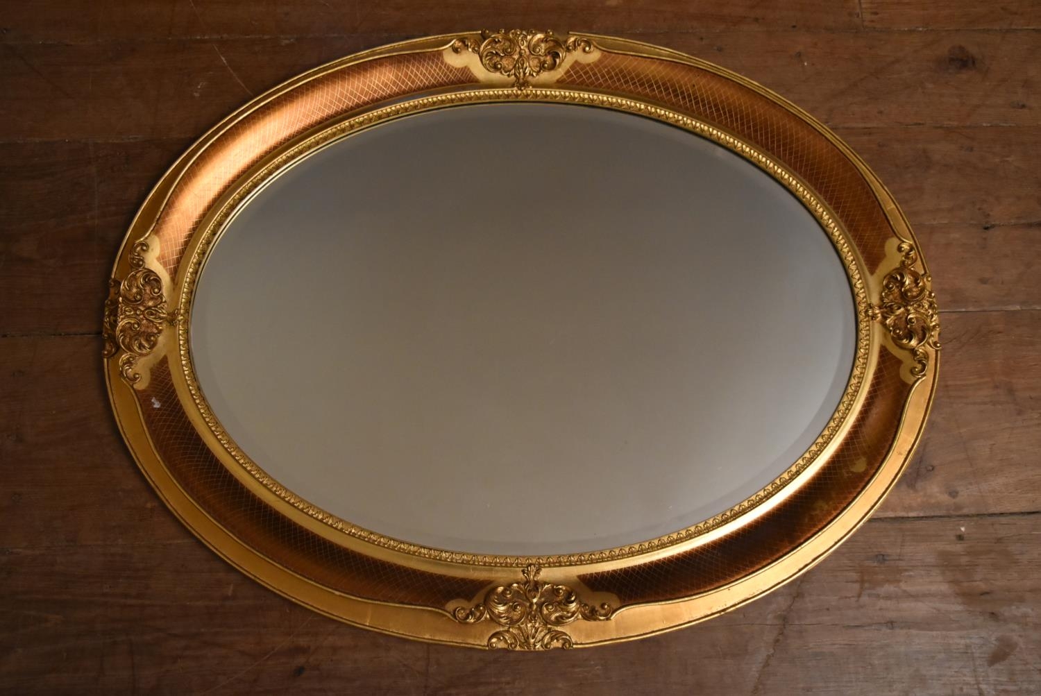A contemporary oval wall mirror in gilt floral decorated frame. H.66 W.86cm