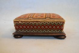 A Victorian mahogany footstool in original tapestry upholstery on squat bun feet. H.15 W.36 D.33cm