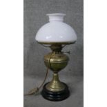 A converted Victorian brass oil lamp with milk glass shade and mounted on a black ceramic base. H.57