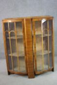 An Art Deco walnut bow front display cabinet, with two curved glazed doors, enclosing shelves,