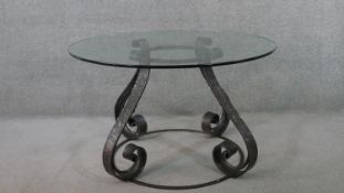 A wrought iron dining table, with a circular plate glass top, on scrolling supports with a