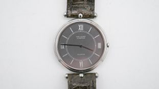 A cased Van Cleef & Arpels watch with black dial with roman numerals, steel case on an grey