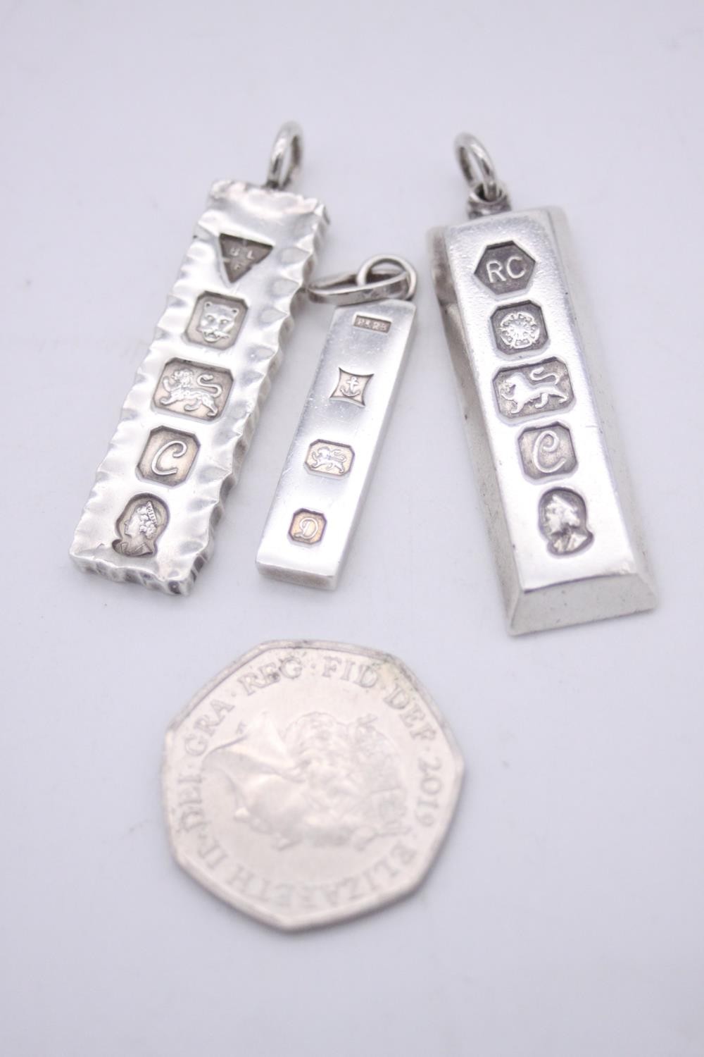 Three silver ingot pendants, each stamped to the front with a different set of hallmarks. Makers: