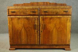 An Art Deco figured walnut sideboard, with a shaped gallery over two short drawers, above two