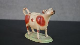 A 19th century Staffordshire pottery hand painted creamer modelled as a cow on grass base. H.13 W.