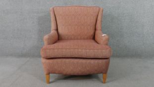 An armchair, upholstered in patterned pink fabric, with scrolling arms, on square section tapering