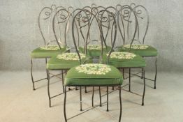 A set of six wrought iron dining chairs with green embroidered seats centred by a floral design.
