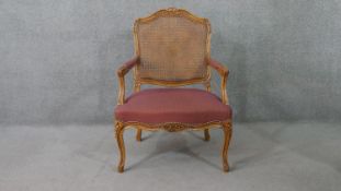 A Louis XVI style beech fauteuil armchair, with a caned back, the arms and seat upholstered in