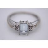 An aquamarine and diamond flanked solitaire ring. Set with an emerald cut aquamarine with an
