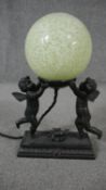 A bronze effect classical design table lamp of two cherubs holding a pale green marbled glass