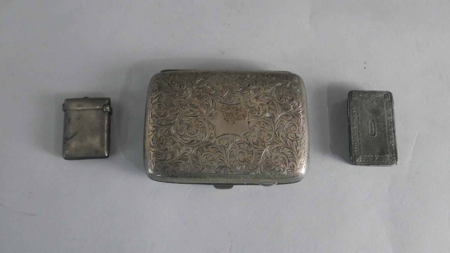 A silver vesta case, an engraved foliate design silver cigarette case and a pewter snuff box.