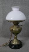 A converted Victorian brass oil lamp with milk glass shade and mounted on a black ceramic base. H.57
