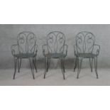 A set of three wrought iron garden chairs, with scrollwork to the back and arms, on a circular