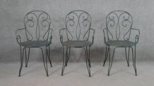 A set of three wrought iron garden chairs, with scrollwork to the back and arms, on a circular