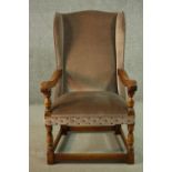 An oak wainscot style wingback armchair, upholstered in brown velour with studded detail, with