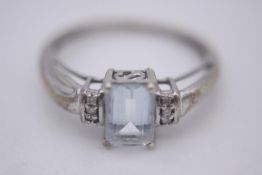 An aquamarine and diamond flanked solitaire ring. Set with an emerald cut aquamarine with an