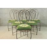 A set of six wrought iron dining chairs with green embroidered seats centred by a floral design.