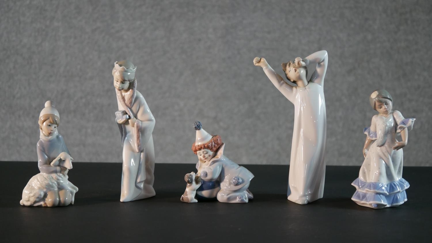 A collection of five Lladro porcelain figures, including a clown and puppy, girl with a lamb, boy in