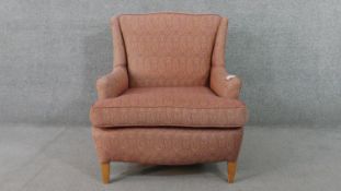 An armchair, upholstered in patterned pink fabric, with scrolling arms, on square section tapering