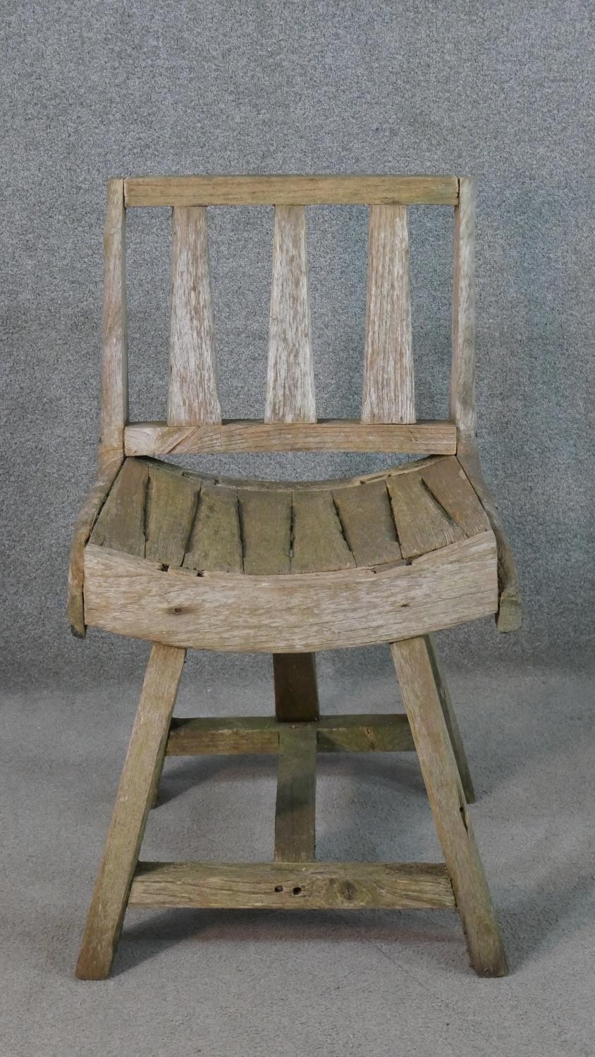 A rustic wooden garden chair, the three splat back over a curved slatted seat, the legs joined by an
