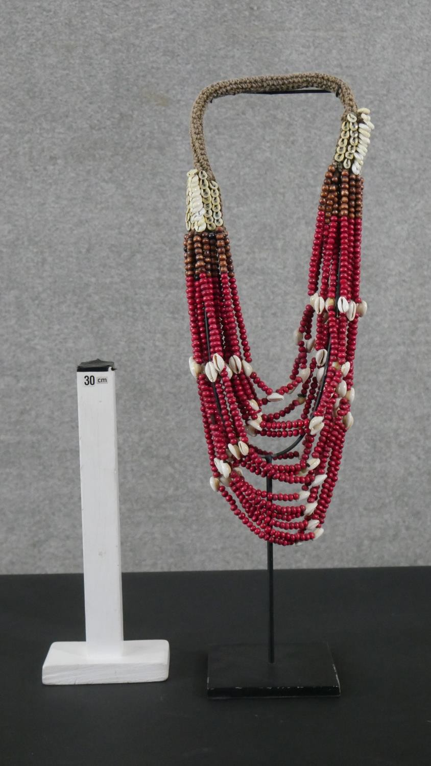 A tribal wooden bead and cowrie shell multi stranded necklace on metal display stand. H.56 W.12 D. - Image 2 of 5