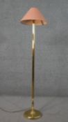A brass standard lamp, with a salmon coloured shade, on a cylindrical reeded and turned stem with