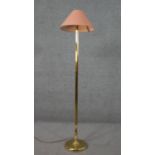 A brass standard lamp, with a salmon coloured shade, on a cylindrical reeded and turned stem with