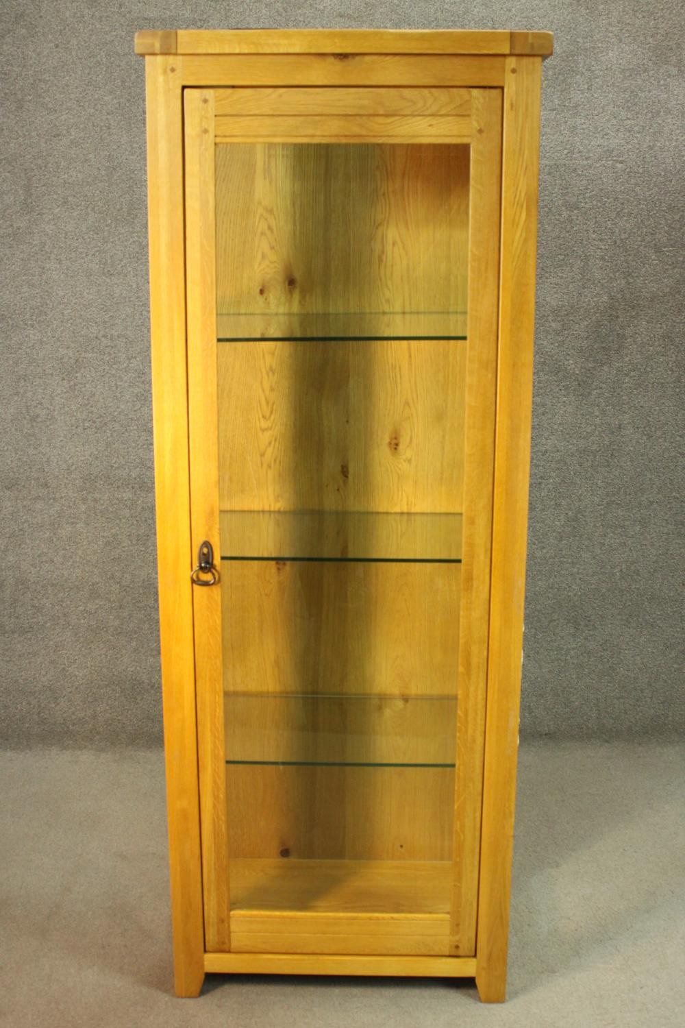 A contemporary honey oak display cabinet, with glazed door and sides, enclosing glass shelves. H.180