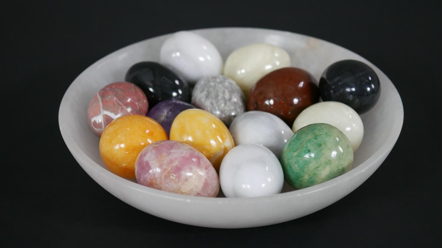 A collection of sixteen egg-shaped hand coolers, various gemstones and minerals in a carved white