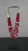 A tribal wooden bead and cowrie shell multi stranded necklace on metal display stand. H.56 W.12 D.