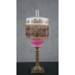 A 19th century brass oil lamp, with an ornate brass column base, opaque pink glass font and an