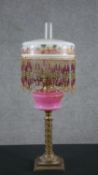 A 19th century brass oil lamp, with an ornate brass column base, opaque pink glass font and an