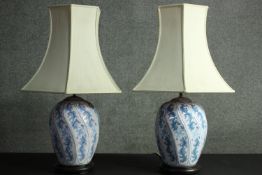 A pair of Chinese style floral design hand painted porcelain lamps on ebonised bases with cream silk