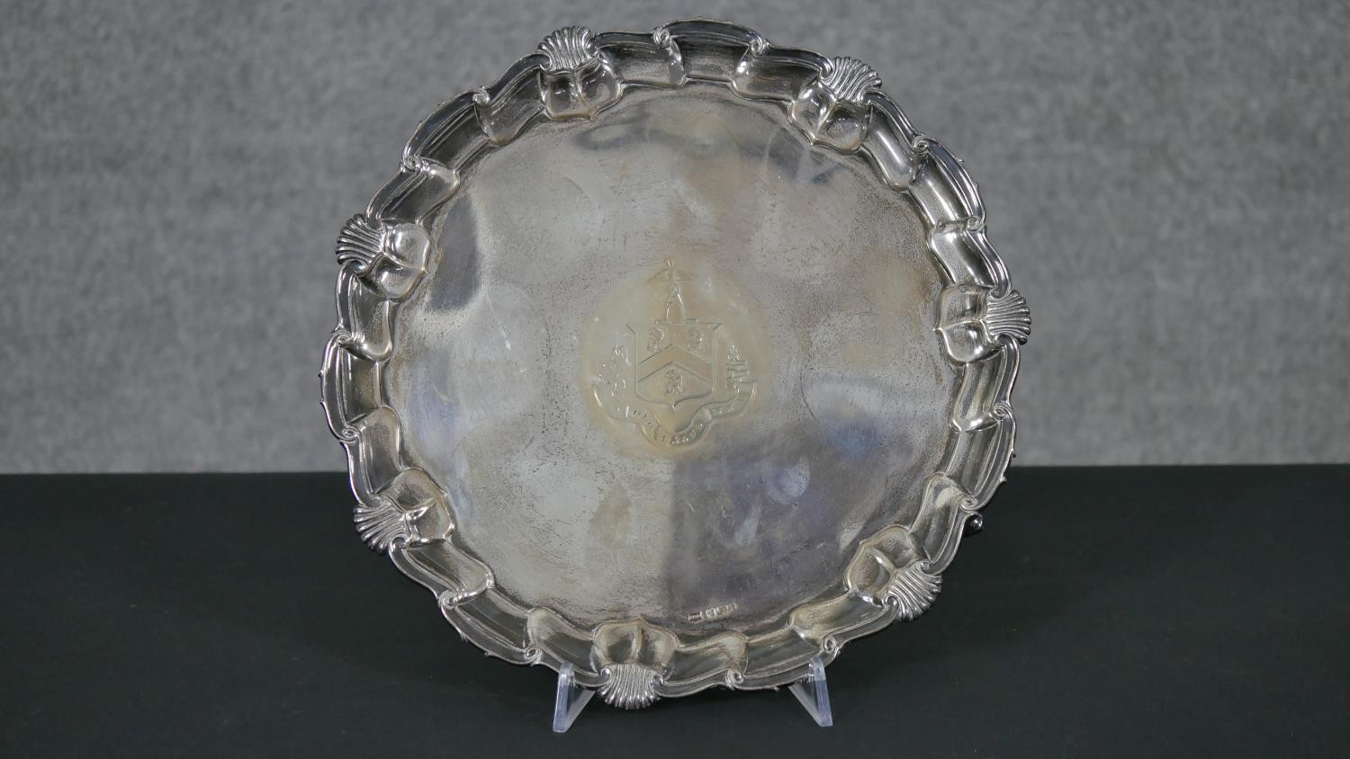 A circular silver salver with shell and scroll border, engraved with crest and motto, on three