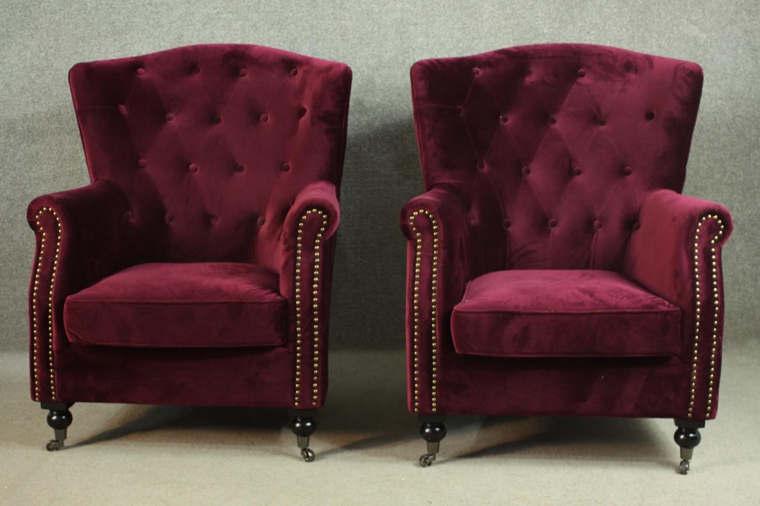 A pair of Victorian style wingback armchairs, upholstered in purple velour, with a buttoned back,