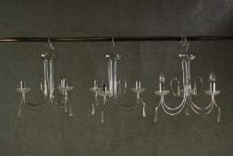 A set of three contemporary chrome chandeliers, each with three curved branches and glass drip