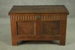 A small 18th century oak coffer, with a plank top over a gouge carved frieze, above two panels, on