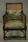 An early 20th century oak bergere armchair, with a caned back and arms, the seat and loose cushion