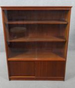 A circa 1960s teak cabinet, with shelves behind a pair of sliding glass doors, over two sliding