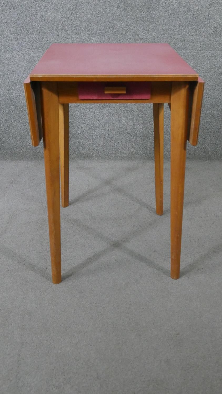 A 1950s drop leaf beech kitchen table, with a pink formica top and a single end drawer. H.78 W.47