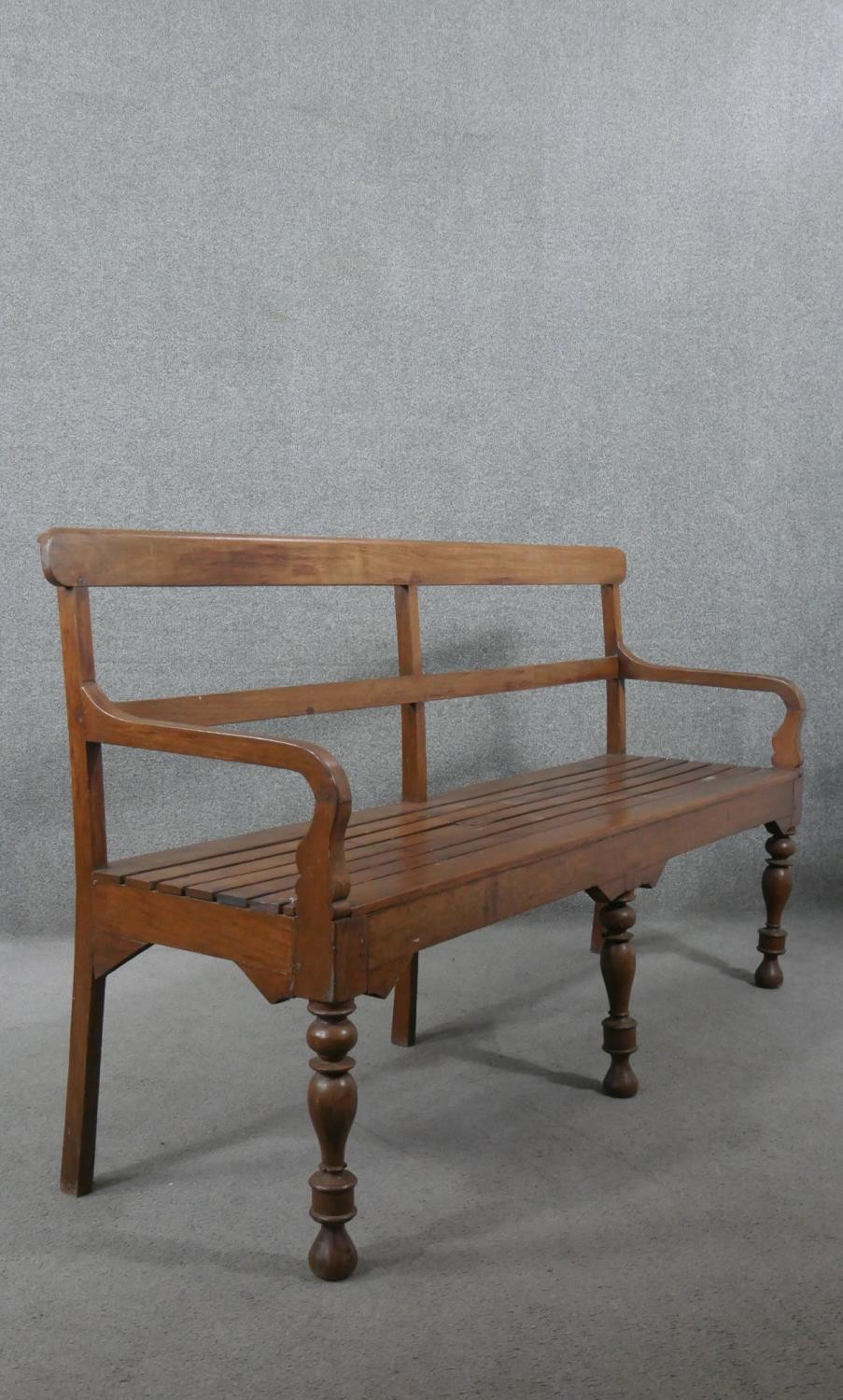 An Indian teak bench, with a bar back and open arms, over a slatted seat, on turned legs. H.93 W.165 - Image 6 of 6