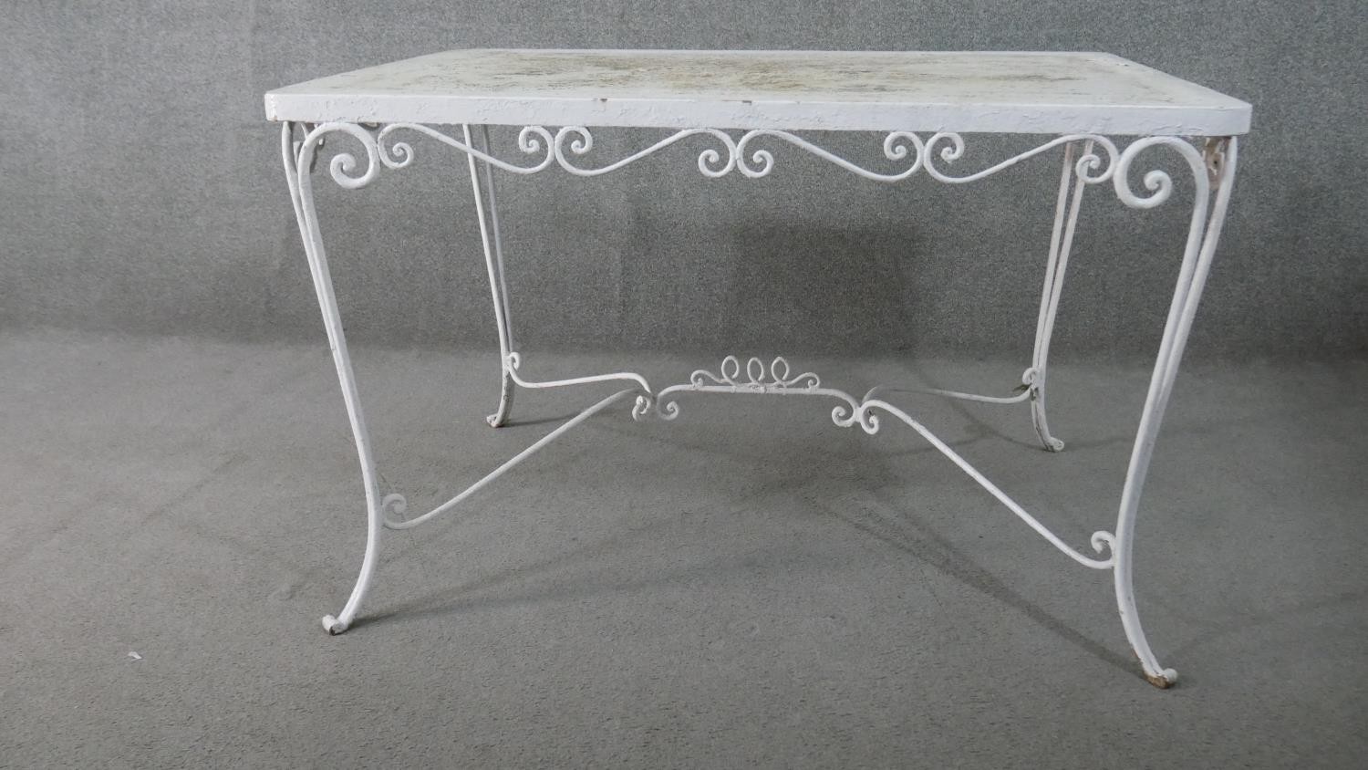 A white painted wrought iron garden table, of rectangular form with scrolling detail, the
