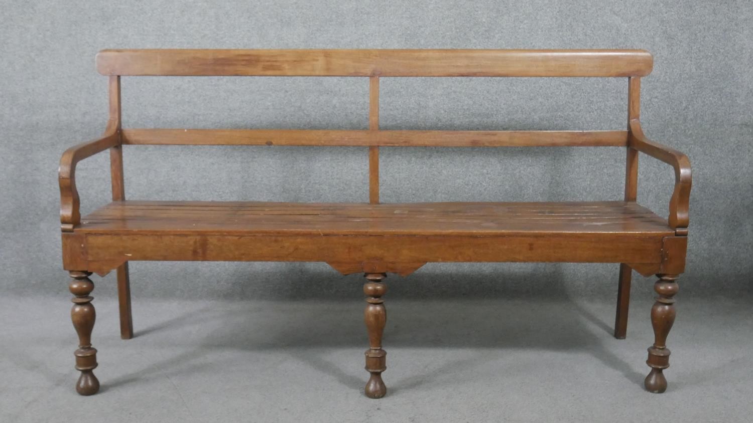 An Indian teak bench, with a bar back and open arms, over a slatted seat, on turned legs. H.93 W.165