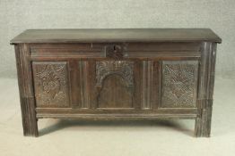 A 17th century and later oak coffer, with a plank top, over three carved panels, with oak handles to