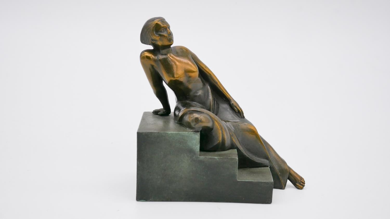 An Art Deco style patinated bronze of a woman reclining on steps. Unsigned. H.15 W.15 D.8cm